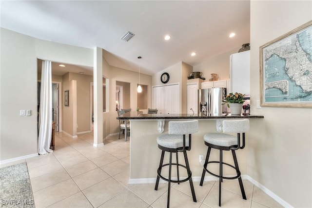 kitchen featuring kitchen peninsula, stainless steel fridge, decorative light fixtures, white cabinetry, and light tile patterned floors