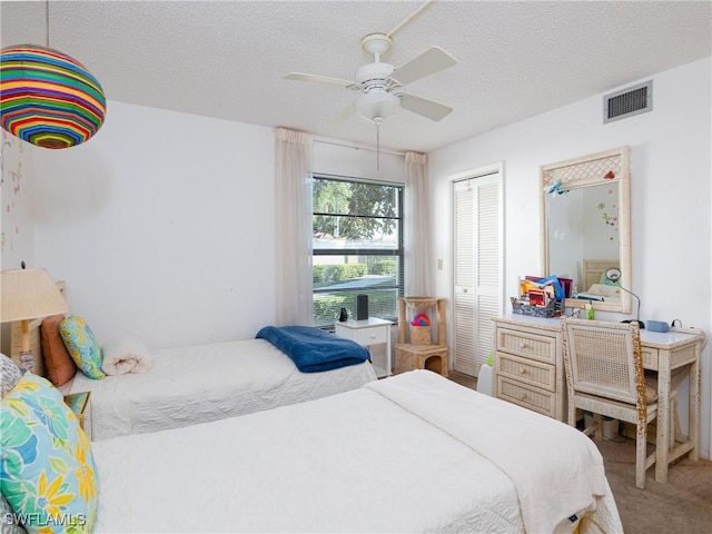 carpeted bedroom with ceiling fan, a textured ceiling, and a closet