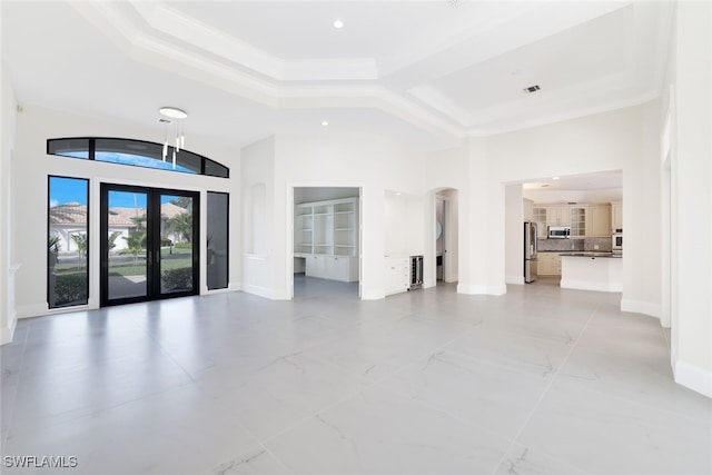 unfurnished living room featuring ornamental molding, french doors, a raised ceiling, and a high ceiling