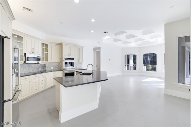 kitchen with coffered ceiling, sink, stainless steel double oven, cream cabinets, and decorative backsplash