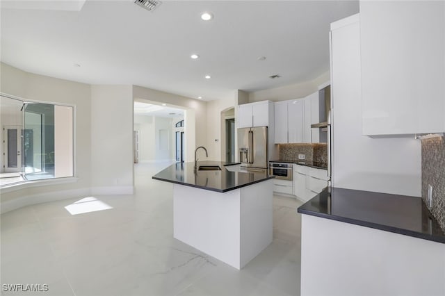 kitchen with appliances with stainless steel finishes, white cabinetry, sink, decorative backsplash, and a kitchen island with sink