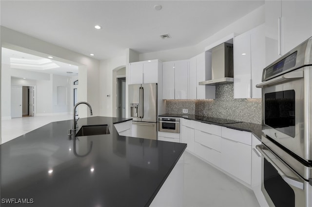 kitchen featuring wall chimney exhaust hood, sink, tasteful backsplash, stainless steel appliances, and white cabinets