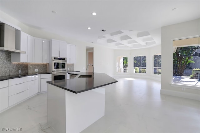 kitchen with wall chimney range hood, sink, stainless steel double oven, and white cabinets