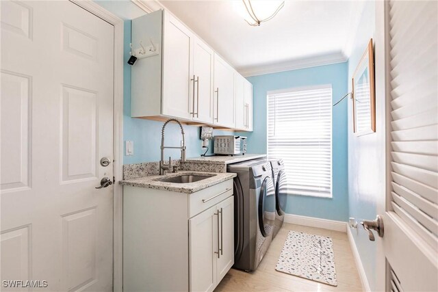 washroom featuring cabinet space, ornamental molding, a sink, separate washer and dryer, and baseboards