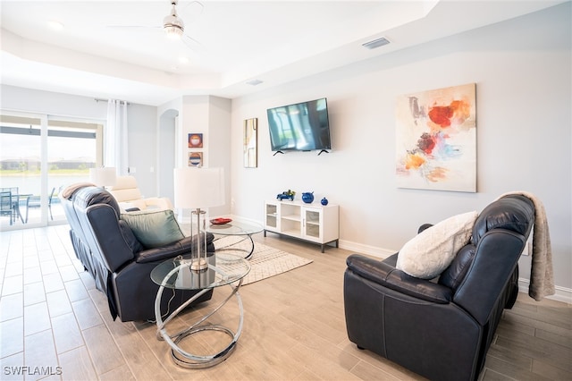 living room featuring a raised ceiling, ceiling fan, and light wood-type flooring