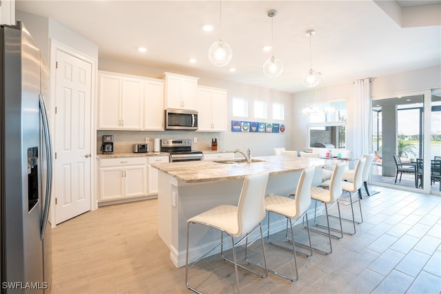 kitchen with white cabinetry, appliances with stainless steel finishes, decorative light fixtures, and a center island with sink