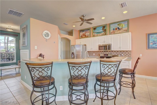 kitchen featuring light tile patterned flooring, appliances with stainless steel finishes, white cabinetry, a kitchen bar, and decorative backsplash