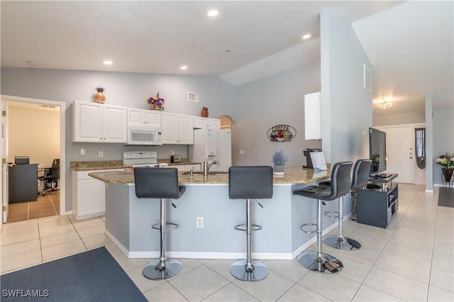 kitchen featuring a kitchen breakfast bar, light stone counters, white appliances, vaulted ceiling, and white cabinets