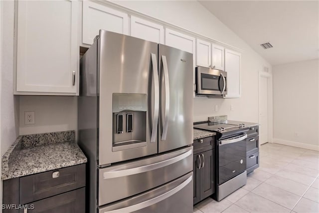 kitchen featuring white cabinets, vaulted ceiling, light stone countertops, light tile patterned floors, and stainless steel appliances