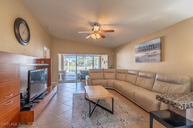 living room with ceiling fan, light tile patterned floors, and vaulted ceiling