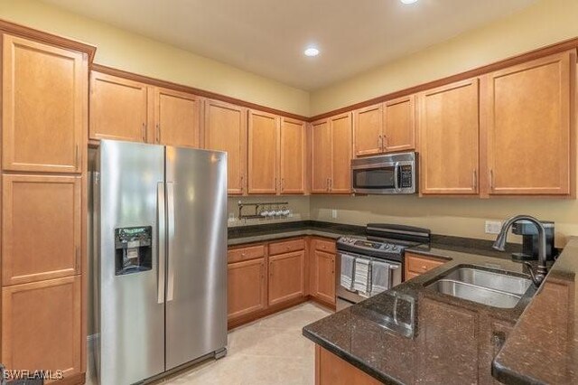 kitchen with stainless steel appliances, dark stone countertops, and sink