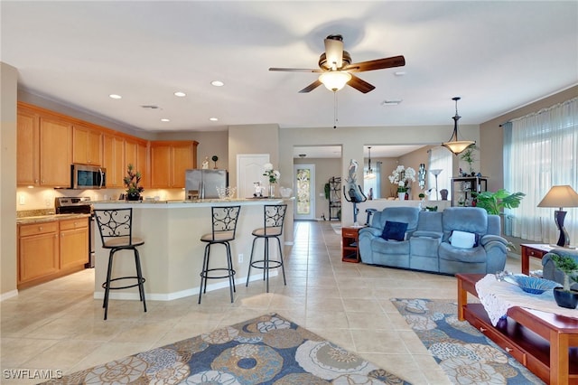 kitchen with appliances with stainless steel finishes, a kitchen island with sink, a kitchen bar, decorative light fixtures, and light tile patterned flooring