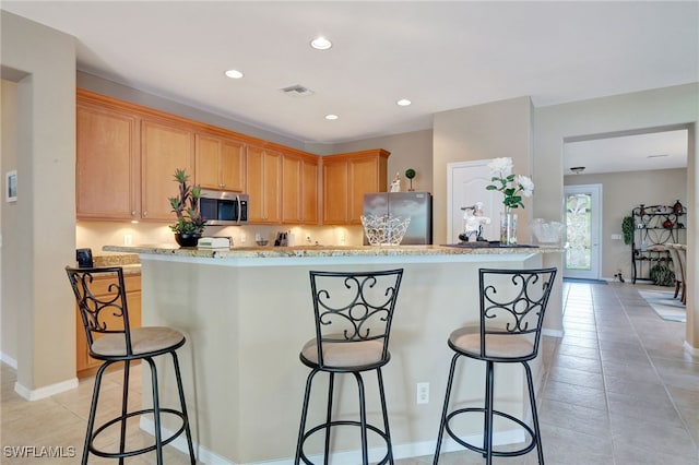 kitchen with light brown cabinetry, a kitchen bar, stainless steel appliances, and light tile patterned flooring