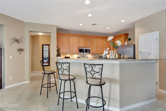 kitchen with stainless steel appliances, light stone countertops, a breakfast bar, and light tile patterned floors