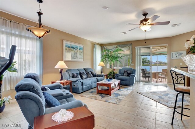 tiled living room with ceiling fan, a healthy amount of sunlight, and a water view