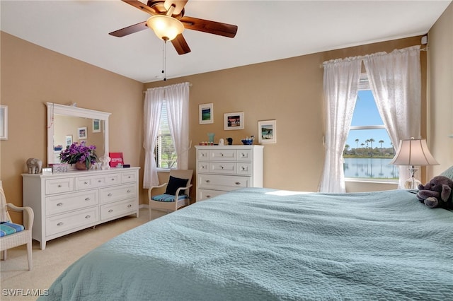 bedroom featuring multiple windows, a water view, light carpet, and ceiling fan