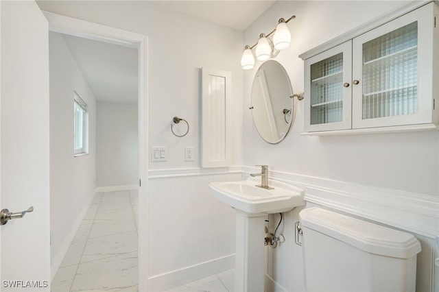 bathroom with toilet, marble finish floor, and baseboards