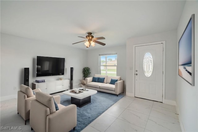 living area featuring a ceiling fan, marble finish floor, and baseboards