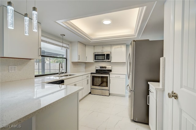 kitchen with white cabinets, a tray ceiling, stainless steel appliances, pendant lighting, and a sink