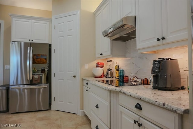 kitchen featuring tasteful backsplash, stainless steel refrigerator, light stone countertops, and white cabinets