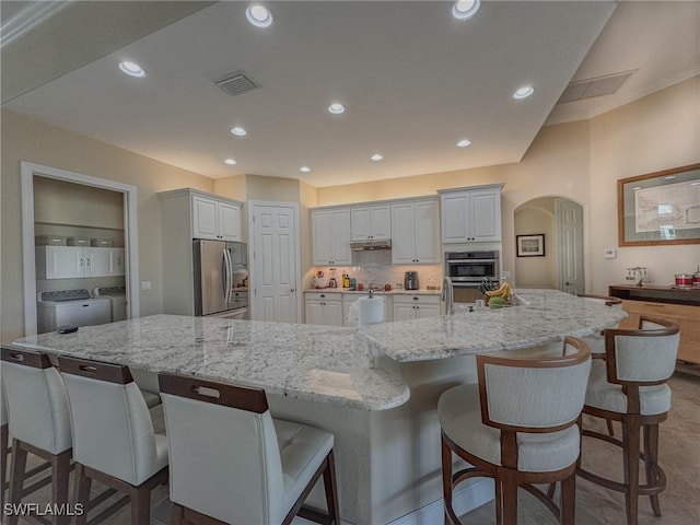 kitchen featuring white cabinets, stainless steel appliances, washer and dryer, and a spacious island