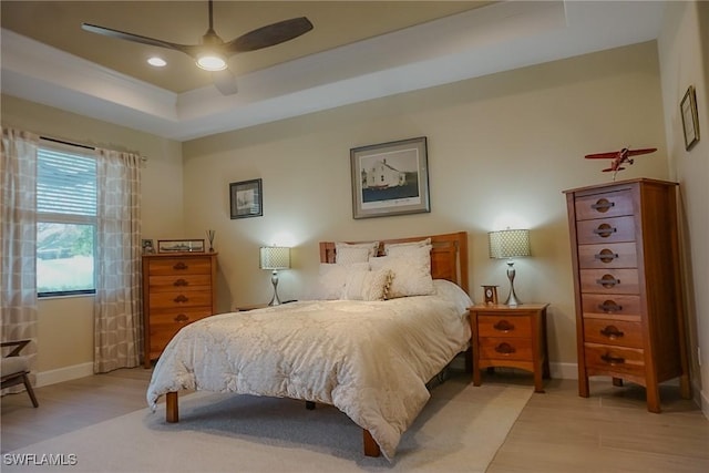 bedroom featuring ceiling fan, a raised ceiling, and light hardwood / wood-style flooring