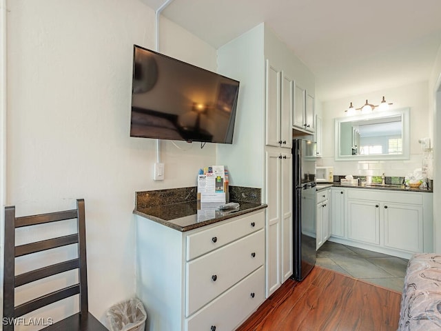 kitchen featuring dark hardwood / wood-style flooring, refrigerator, dark stone counters, sink, and white cabinetry