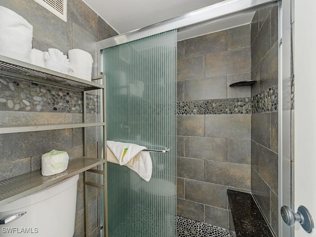 bathroom featuring a shower with door and toilet