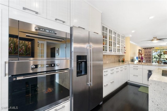 kitchen featuring light stone counters, kitchen peninsula, decorative backsplash, white cabinets, and appliances with stainless steel finishes