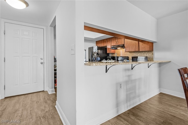 kitchen with a kitchen breakfast bar, backsplash, kitchen peninsula, light hardwood / wood-style floors, and black refrigerator