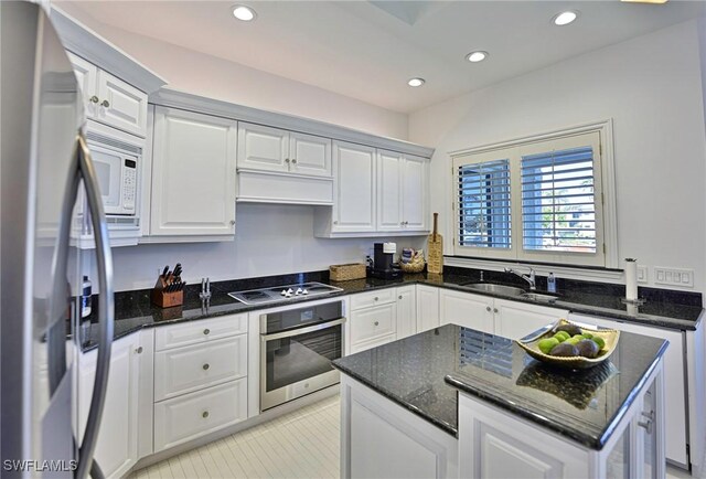 kitchen featuring stainless steel appliances, dark stone countertops, white cabinets, and sink