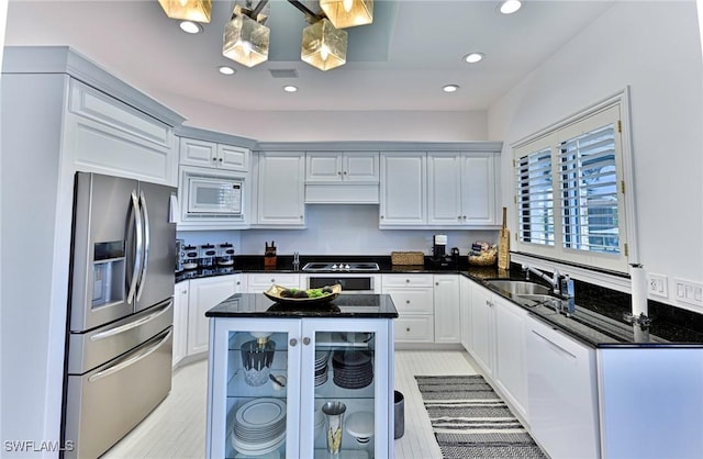 kitchen with dark stone countertops, a center island, stainless steel refrigerator with ice dispenser, sink, and white microwave