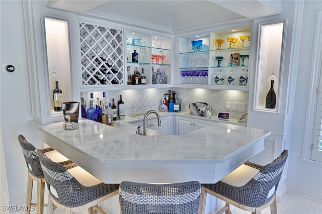 bar featuring light tile patterned floors, backsplash, light stone countertops, white cabinets, and sink