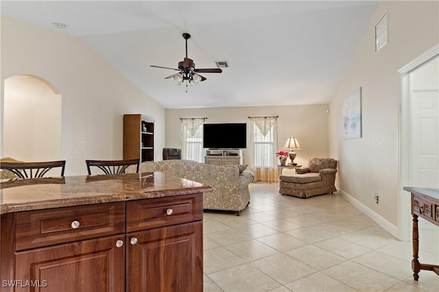 kitchen with ceiling fan, light stone counters, light tile patterned floors, and vaulted ceiling