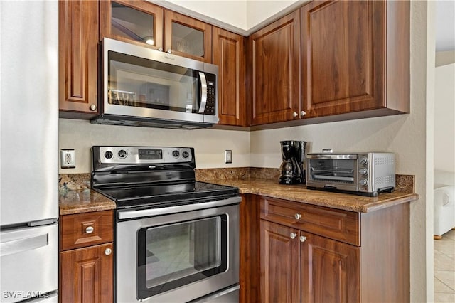 kitchen with light tile patterned flooring, dark stone countertops, and stainless steel appliances