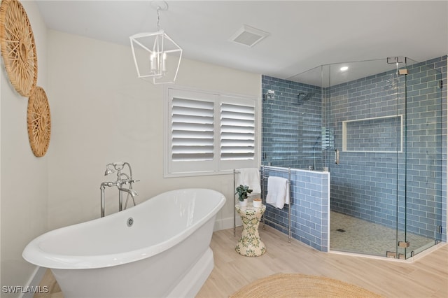 bathroom featuring plus walk in shower, a chandelier, and hardwood / wood-style flooring