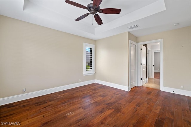 empty room featuring dark hardwood / wood-style flooring, a tray ceiling, and ceiling fan