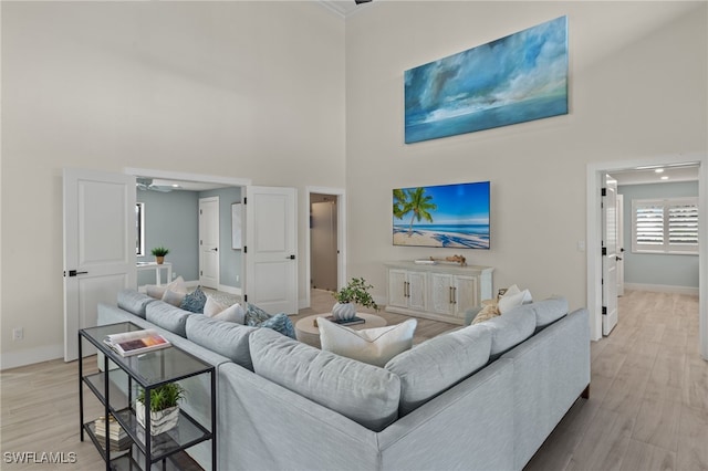 living room with ceiling fan, light hardwood / wood-style floors, and a high ceiling