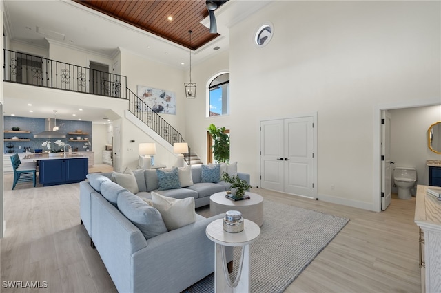 living room featuring ceiling fan, crown molding, a towering ceiling, wood ceiling, and light wood-type flooring