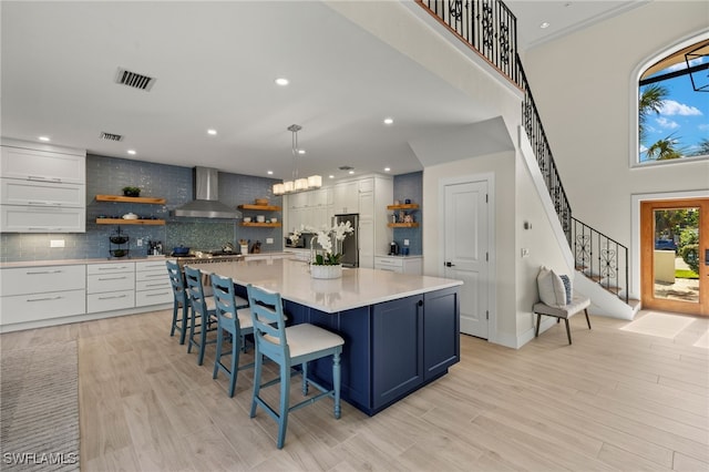 kitchen featuring white cabinets, wall chimney range hood, a large island, a kitchen bar, and stainless steel refrigerator