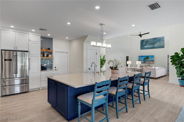 kitchen with high quality fridge, white cabinetry, sink, and a large island