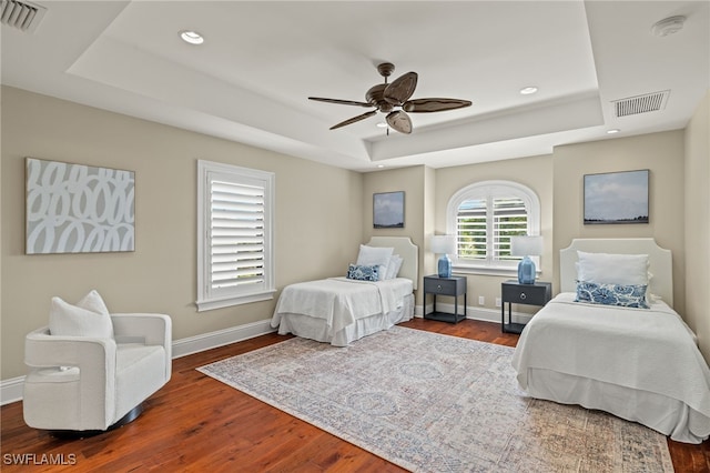 bedroom featuring ceiling fan, dark wood-type flooring, and a tray ceiling