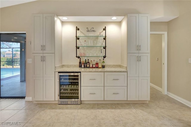 bar featuring light tile patterned floors, light stone counters, white cabinetry, and beverage cooler