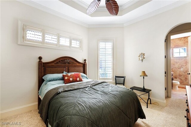 bedroom featuring a raised ceiling, ensuite bath, light carpet, ceiling fan, and ornamental molding