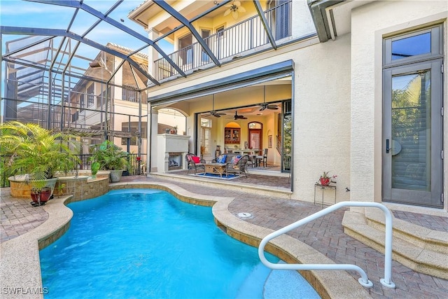 view of swimming pool featuring ceiling fan, a patio, exterior fireplace, and glass enclosure