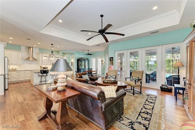 living room featuring a tray ceiling, ceiling fan, french doors, and light hardwood / wood-style flooring