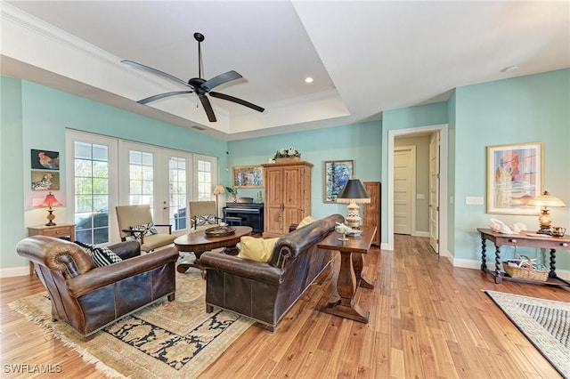 living room with french doors, a raised ceiling, crown molding, light hardwood / wood-style flooring, and ceiling fan