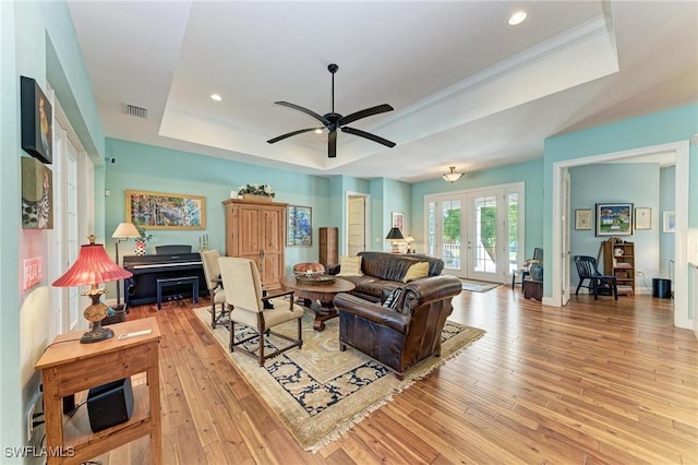 living room featuring french doors, light hardwood / wood-style flooring, a raised ceiling, and ceiling fan