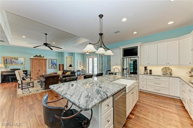 kitchen with a tray ceiling, white cabinetry, a center island with sink, and appliances with stainless steel finishes