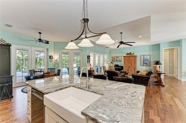 kitchen featuring french doors, sink, light stone counters, stainless steel dishwasher, and pendant lighting